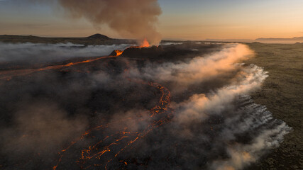 Aerial view of fiery rivers of molten lava snake through a stark, volcanic landscape, contrasting with ethereal veils of mist near Grindavikurber, Reykjanes, Iceland.
