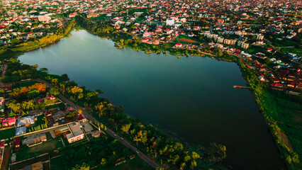 Aerial view of the serene lake reflects the sky, bordered by lush greenery and vibrant buildings, creating a peaceful contrast, Ilorin, Kwara, Nigeria.
