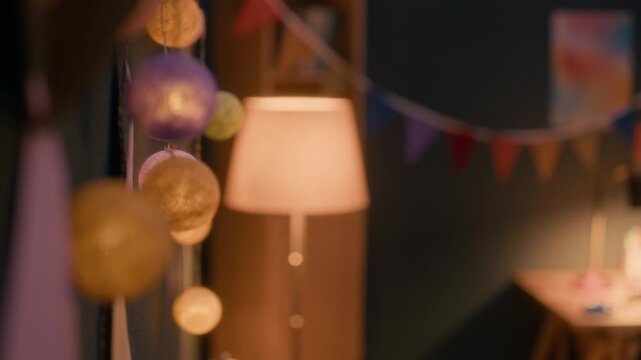 No people interior shot of warmly lit child study area with cotton ball string lights, colorful bunting, wooden desk, cactus neon light, and creative decor in cozy bedroom setting