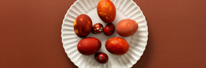 Vibrant Easter eggs in various shades of red and orange are beautifully arranged on a white plate, adding charm to the festive atmosphere of the season, banner