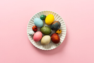 A collection of vibrant Easter eggs in various colors is artfully arranged on a white plate, set against a soft pink background, capturing the essence of the holiday's decorations