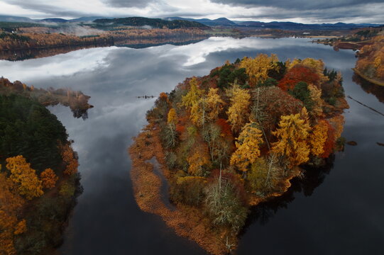Aerial view of an island with vibrant autumn foliage reflected in the still waters of Loch Gynack, a serene scene, Kingussie, Scotland, United Kingdom.