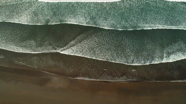 Aerial view of wide ocean waves creating parallel lines on chocolate sandy beach