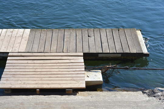 Two wooden floating docks and concrete steps extend down toward the blue, rippling water of a river or lake