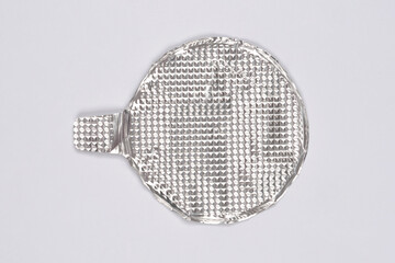A round, textured silver aluminum foil lid with a pull tab is isolated and centered on a plain light gray background