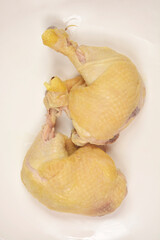 An overhead studio shot features two pale, boiled chicken leg quarters, stripped of skin but still on the bone, presented on a simple white plate.