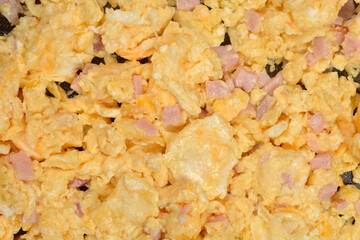 An extremely tight, textured macro shot completely fills the frame with fluffy yellow scrambled eggs mixed with pieces of ham and cheese