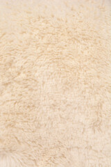 A close-up vertical full-frame shot of a plush, soft, and textured cream or beige faux fur material