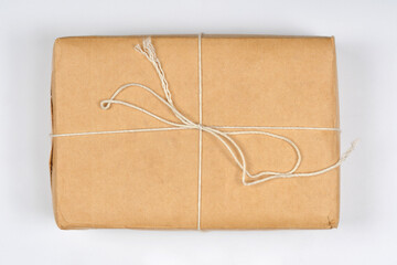 A rectangular package wrapped in plain brown paper and tied with simple white string is centered on a white background