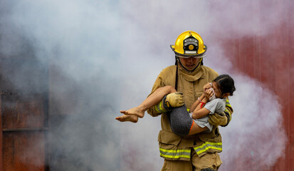 Firefighter in fireproof clothe is carrying young kid out of the burning building full of ash and...