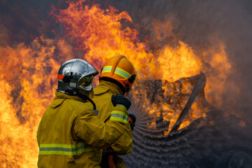 Obraz premium Team of firefighter in fireproof clothe are using twirl fog watering hose to put out the burning building with high flame for fire extinguish risk rescue mission, accident management