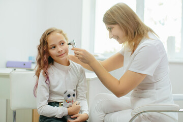 Pediatrician examining young girl's ear with otoscope