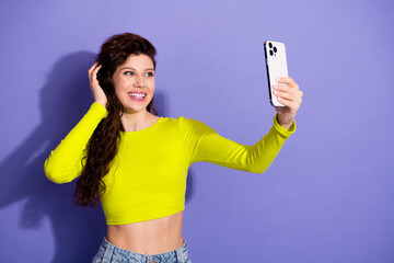 Young woman takes selfie with neon yellow top against purple background showcasing casual fashion lifestyle and cheerful vibe for social media and advertising