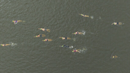 Cape Town, South Africa - 25 October 2025: Aerial view of swimmers cutting through the murky waters, their yellow caps dotting the surface like scattered suns.