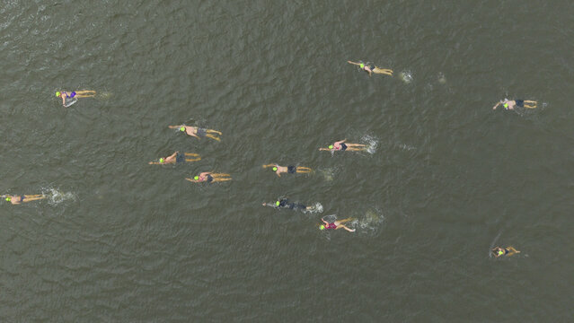 Cape Town, South Africa - 25 October 2025: Aerial view of swimmers cutting through the murky waters, their yellow caps dotting the surface like scattered suns.