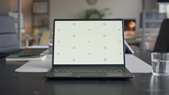 Zoom out shot of chroma key laptop on conference table with stationery and glass of water nearby in modern open space office, set for negotiations or business meeting