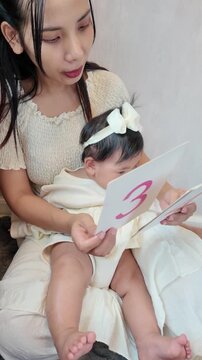 A mother showing number flashcards to her baby in the living room, creating an engaging early learning moment