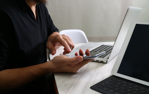 Man using smartphone while working with laptop and tablet