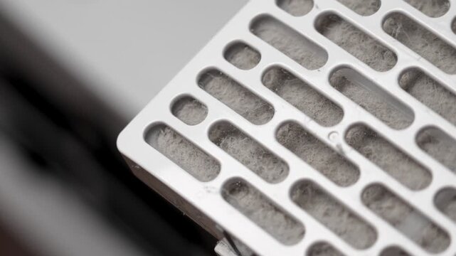Dusty clogged white plastic filter with oval slots on dehumidifier panel background. Home appliance maintenance concept