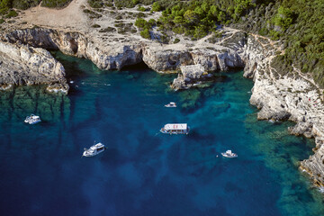 Aerial view of the azure sea meeting the rugged, rocky coastline, punctuated by boats near the cliffs, Pinizule, Istria County, Croatia.