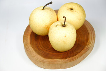 Three round yellow pears are served on a wooden base taken from a three-quarter angle.