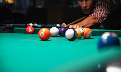 A close-up view of colorful billiard balls scattered on a green felt table while a focused man in a...