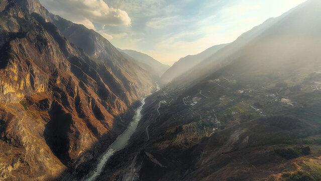 Aerial view of the dramatic Tiger Leaping Gorge, a deep canyon with a river winding through steep, rocky cliffs under a hazy sky, Diqing Tibetan Autonomous Prefecture, Yunnan, China.