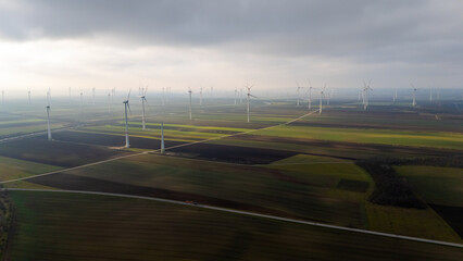 Aerial Drone View of Wind Turbines in Austria. Endless green fields covered with wind farms, morning fog, soft sunlight and sustainable clean energy generation captured from above