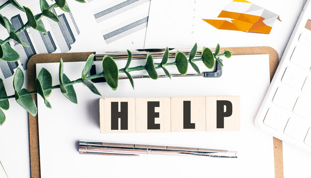 Wooden blocks with word help on clipboard with financial charts, calculator, pen and green leaves
