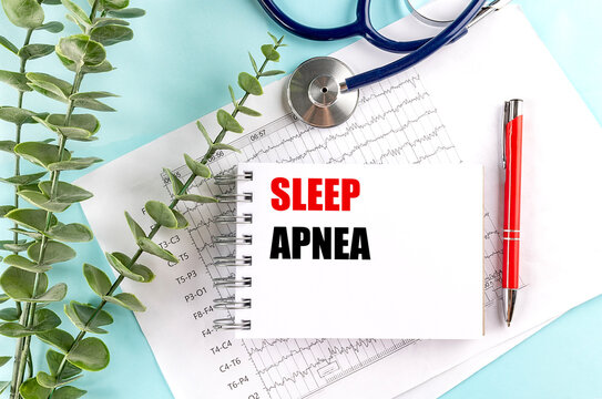 Notepad with text sleep apnea on top of diagnostic charts with stethoscope, red pen and eucalyptus