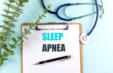 Clipboard with text sleep apnea, next to stethoscope, pen and eucalyptus on blue background