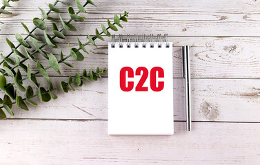 White notepad with red letters C2C placed on wooden desk with green plant and silver pen