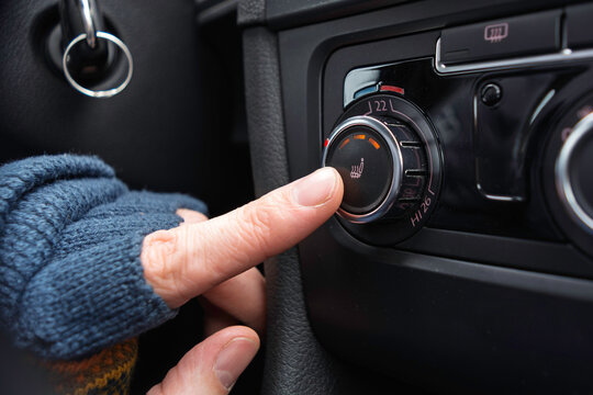 Driver in warm glove presses seat heating button to quickly add warmth inside car during a cold winter ride