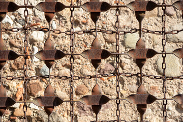 Close-up of a rusty, ornate wrought iron gate or fence against a stone wall. Detailed texture, aged metal, and historic outdoor architectural element