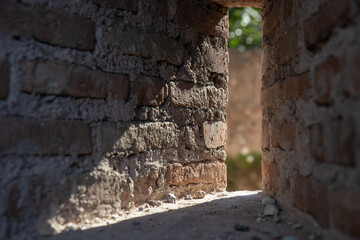 Close-up low-angle view through a narrow opening in a weathered brick wall, revealing a historic ruin or abandoned structure. Texture, decay, and architectural detail