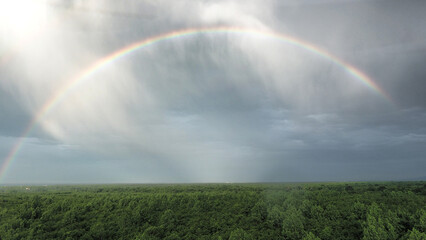 Aerial view of a rainbow arcing across a dramatic sky, contrasting with the lush green forest below, Pir-e Harat, Gilan Province, Iran.
