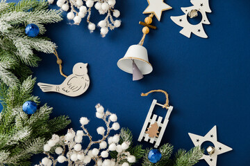 Christmas flat lay with wooden toys, bell, and frosted fir on blue background