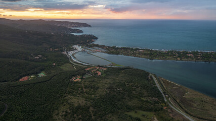 Aerial view of the winding coastline where the Orbetello Lagoon meets the Tyrrhenian Sea under a vibrant sunset, Monte Argentario, Toscana, Italy.
