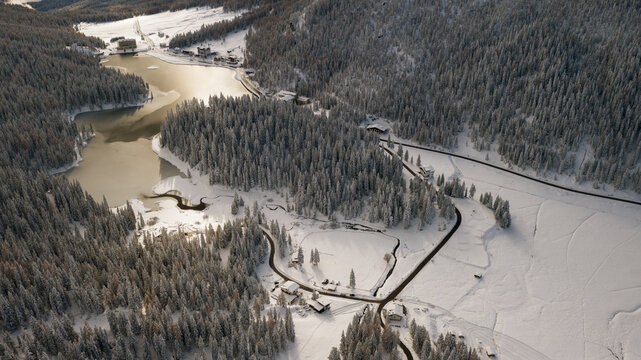 Aerial view of the snow-covered landscape, with a serene lake reflecting the soft light, and roads winding through the frosted trees, Auronzo di Cadore, Veneto, Italy.