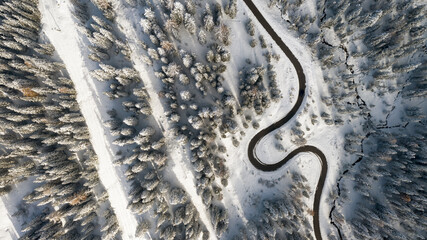 Aerial view of a winding road snaking through a snow-laden forest, a stark contrast of dark asphalt against the pristine white landscape, Passua, Trentino-Alto Adige, Italy.