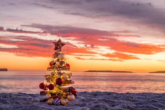Pretty decorated Christmas Tree baubles and fairy lights sunrise beach scene