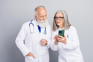 Senior doctors review patient care as elderly man with stethoscope consults while colleague uses smartphone