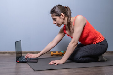 Woman using laptop on floor mat to start an online fitness class or personal remote training session, home workout technology, or modern wellness lifestyle concepts