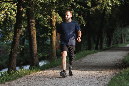 A man walks on a path wearing a prosthetic leg in a park, enjoying the outdoor space during a sunny afternoon. - Powered by Adobe