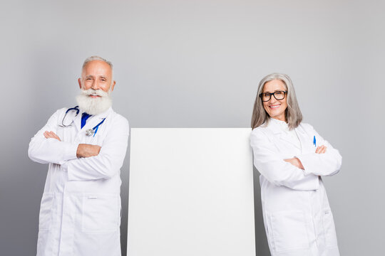 Two experienced doctors in white coats stand with arms crossed smiling beside a blank board for a medical consultation concept - Powered by Adobe