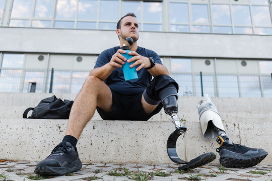 Athlete with leg amputation resting on outdoor steps after workout. Strength, motivation, and healthy living concepts. - Powered by Adobe