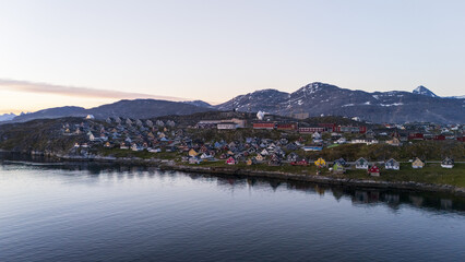 Aerial view of quaint houses dotting the rugged coastline under a serene sky, nestled against the backdrop of snow-capped mountains, Nuuk, Sermersooq Municipality, Greenland.