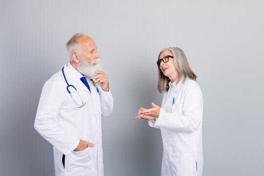 Senior doctors discuss patient care during a medical consultation in white coats with stethoscope against a grey background