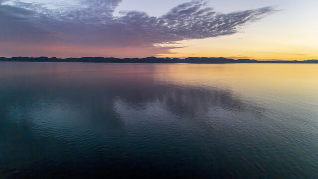 Aerial view of the tranquil waters reflecting the pastel sky above distant, dark land, creating a serene and ethereal atmosphere, Nuuk, Sermersooq Municipality, Greenland.