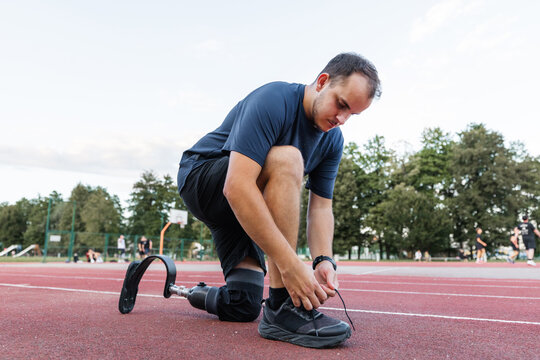Athlete with a disability, wearing a prosthetic running blade, pausing on the track to tie his shoelace on a sneaker. Motivation and persistence concept.